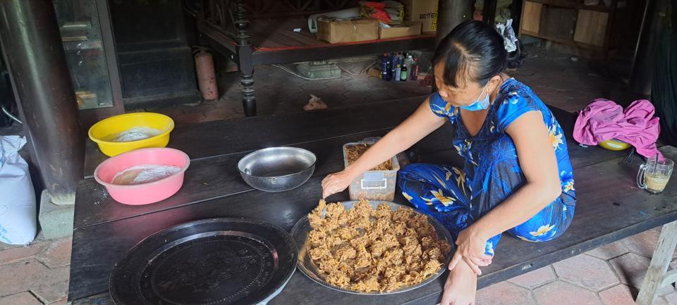 Chị Lê Thị Oanh (con bà Ngỏ) ngồi trên bộ phản gỗ quý để làm bánh in nhân gừng trộn chuối bán cho khách.